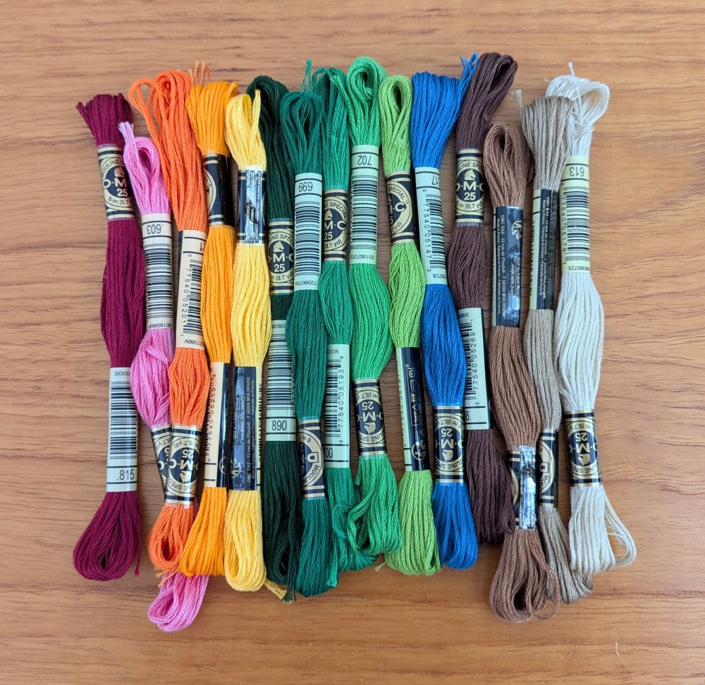 15 skeins of embroidery thread arranged on a table, with reds to the left and then in rainbow order with brown and cream at the right end.