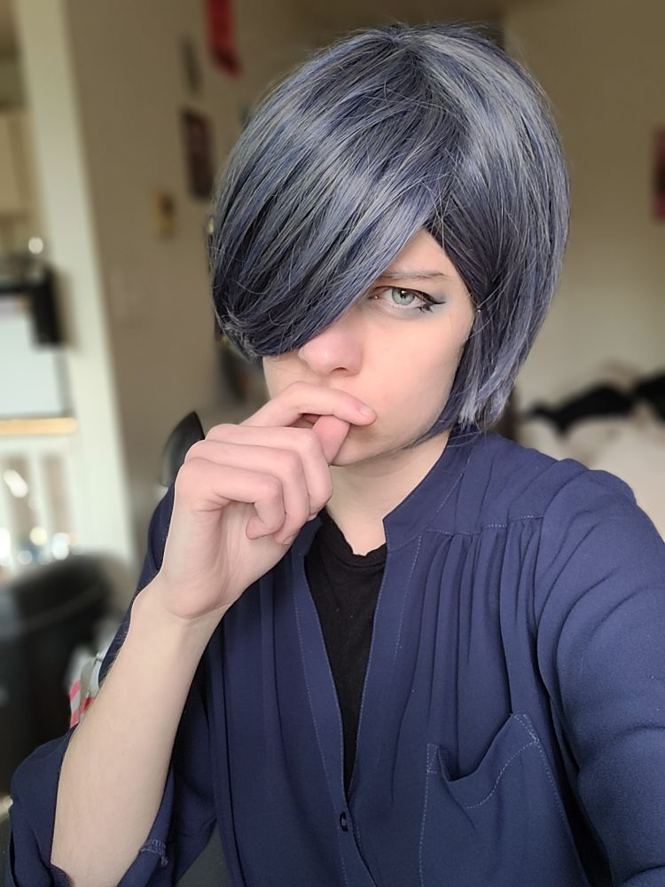 a ciel phantomhive cosplayer wearing a blue buttom up over a black shirt, glaring at the camera with his index finger and thumb covering his mouth