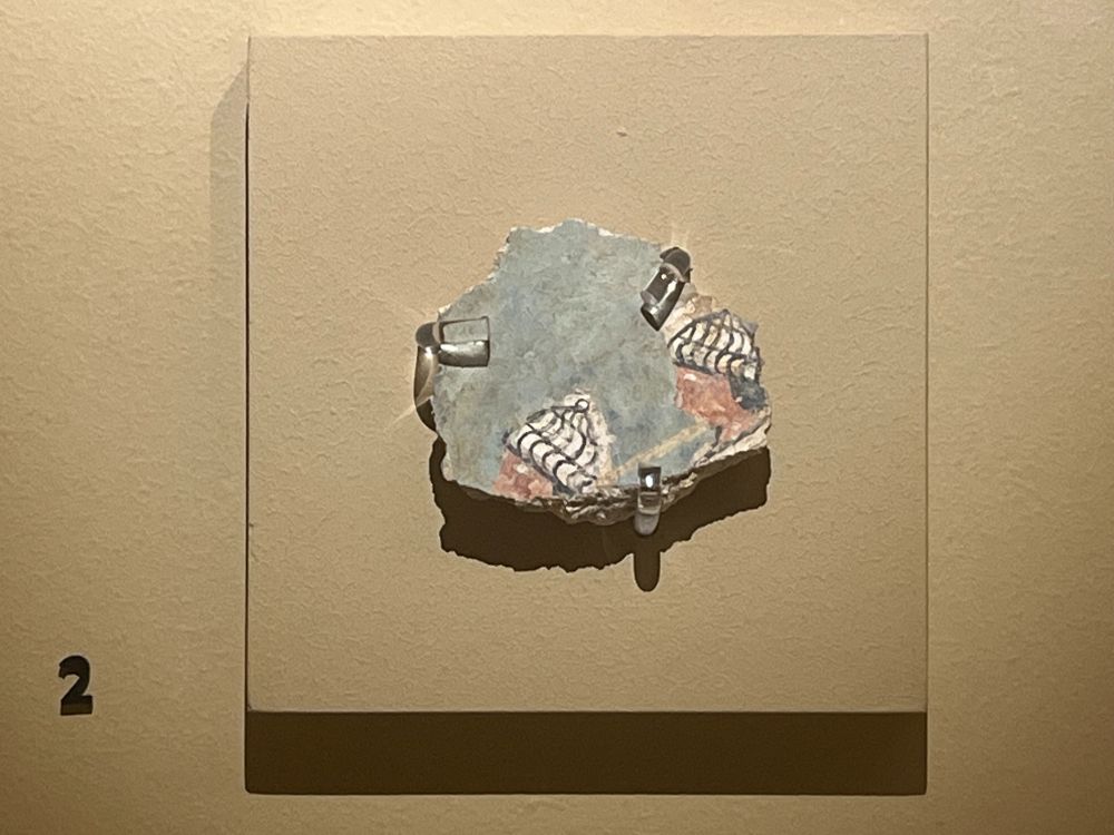 Small fragment of a fresco, with two heads wearing boars-tusk helmets against a light-blue background.