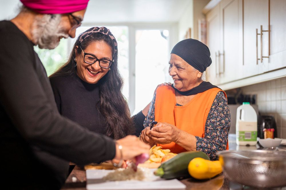 A group of older people smiling in a kitchen as they chop up vegetables for a meal.