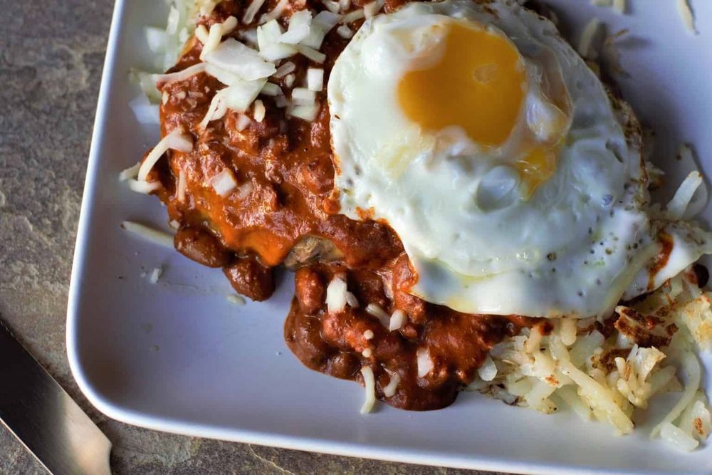 a plate with [deep breath] hashbrowns topped with a burger patty topped with chili topped with diced onions + cheese topped with a sunny egg 