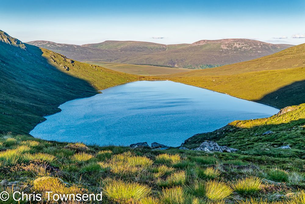 A loch in the hills in bright evening light under a clear sky.