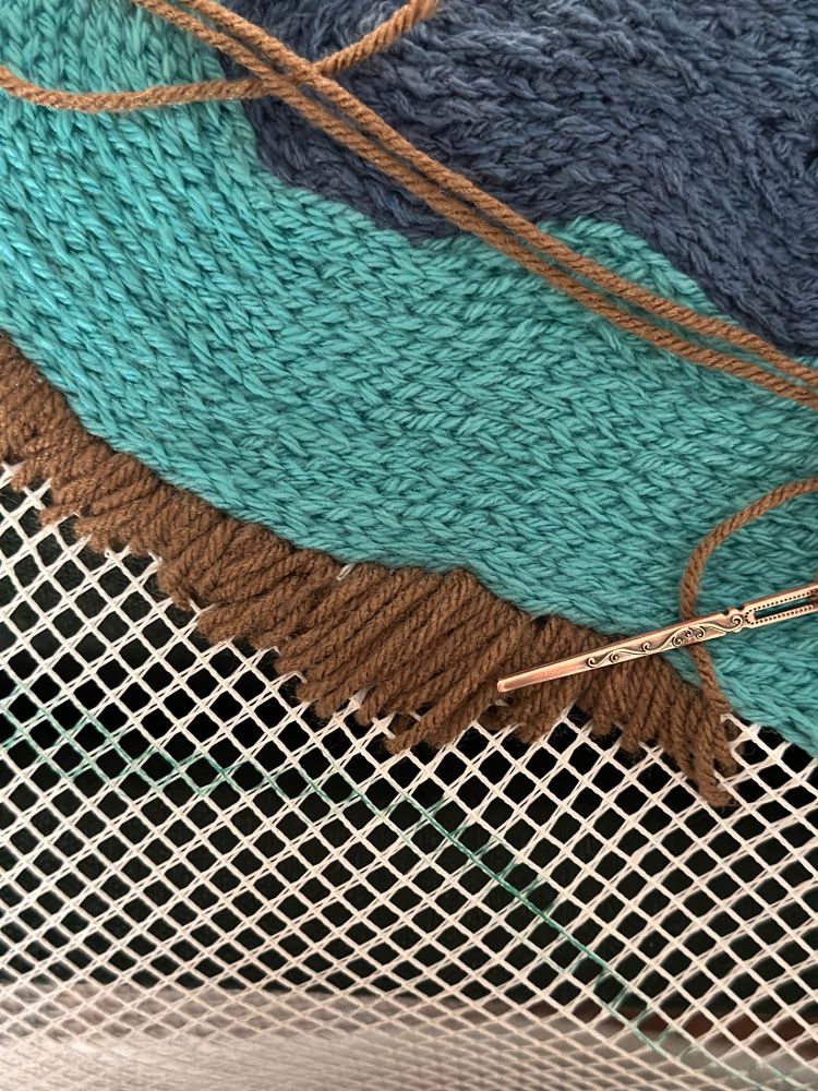 Blue and light blue yarn crocheted in an ovular shape with brown yarn in the process of being stitched on 