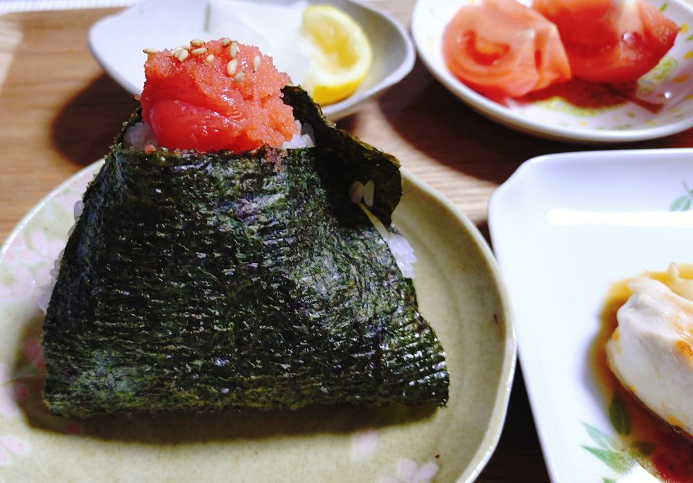 2025/12/11　の晩ごはんの写真1枚目。
主食のおにぎり。炊きたての新米に甘口たらこを合わせて、海苔で巻いたもの。おにぎりの三角形の上部分にたらこを少し見えるように乗せて、炒りごまをトッピングしてある。