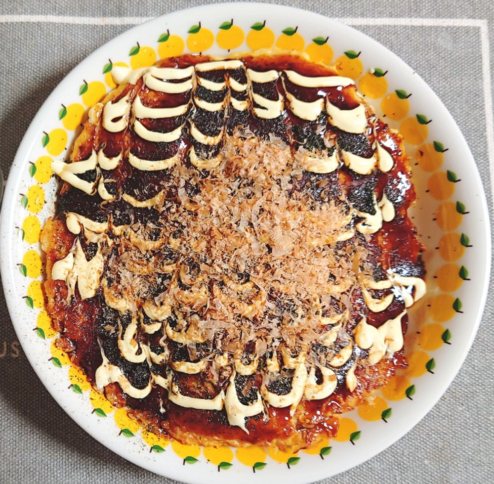 昼食の写真。オートミールで作ったお好み焼き2人前を3人で分けるところ。丸い大皿に盛られている。
ソース、マヨネーズ、青のり、かつお節をトッピング。
