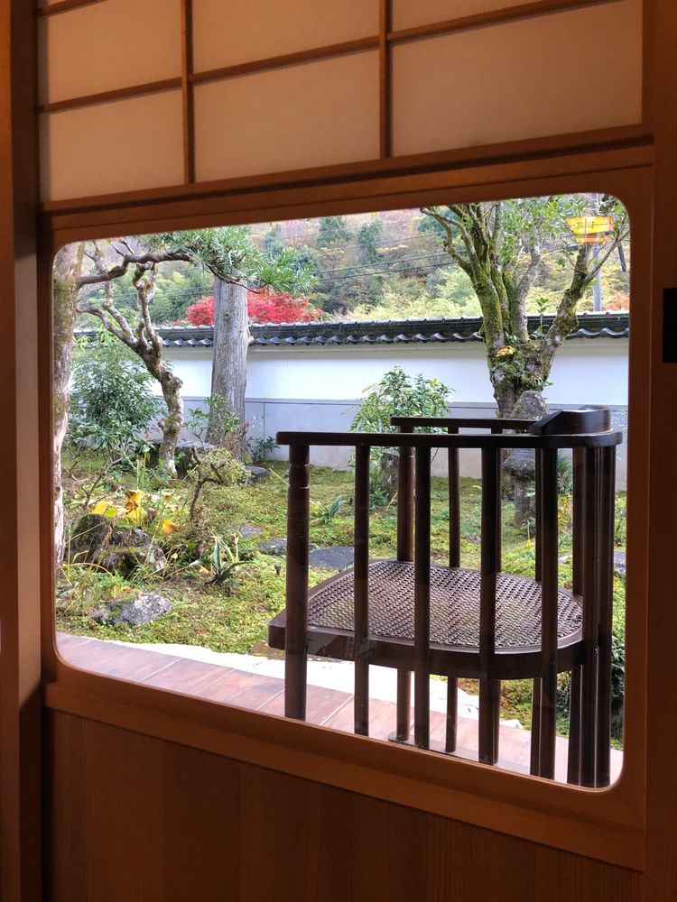 View through a sliding door into a Japanese garden. There is a lacquered bamboo chair on the walkway.