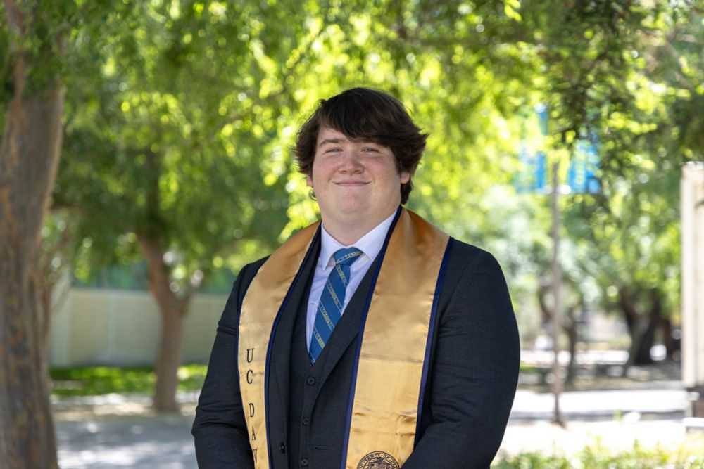 Buttery stands outdoors wearing UC Davis stole