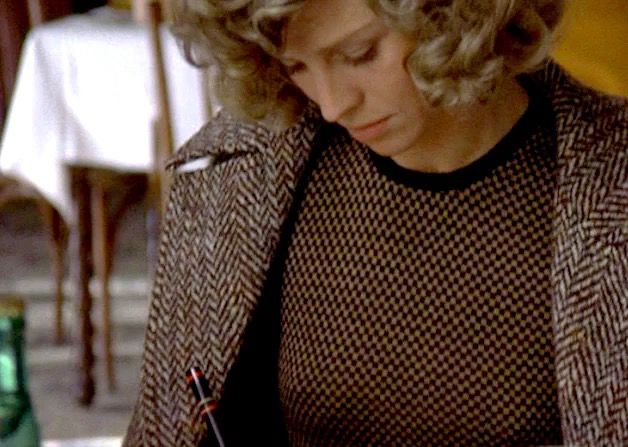 Julie Christie wearing a brown tweed coat and black and brown checked sweater. 