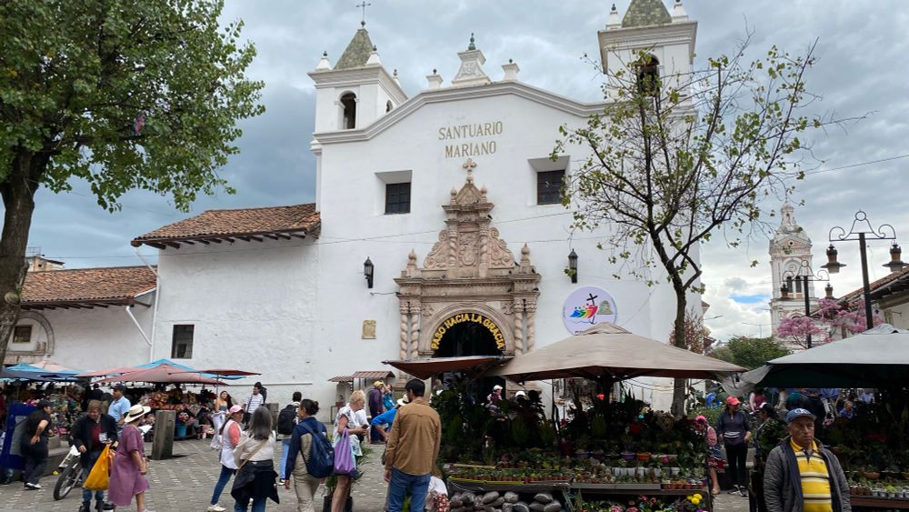 a flower market fills the plaza of a large white church