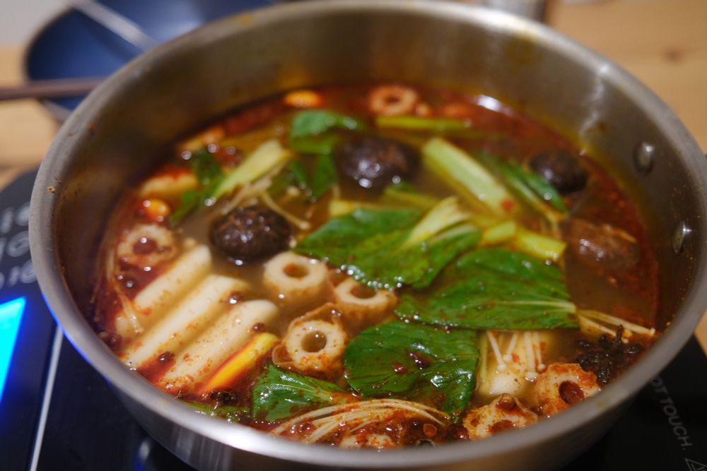 A close up of a hotpot soup with fish cakes, enoki and shiitake mushrooms, rice cakes and bok choy. 