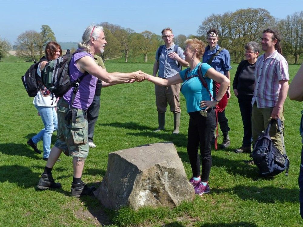 Two hikers shaking hands over a boulder. 