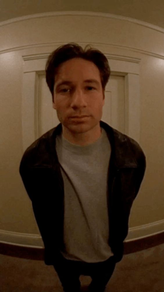 a man wearing a leather jacket and a grey shirt is standing in front of a door