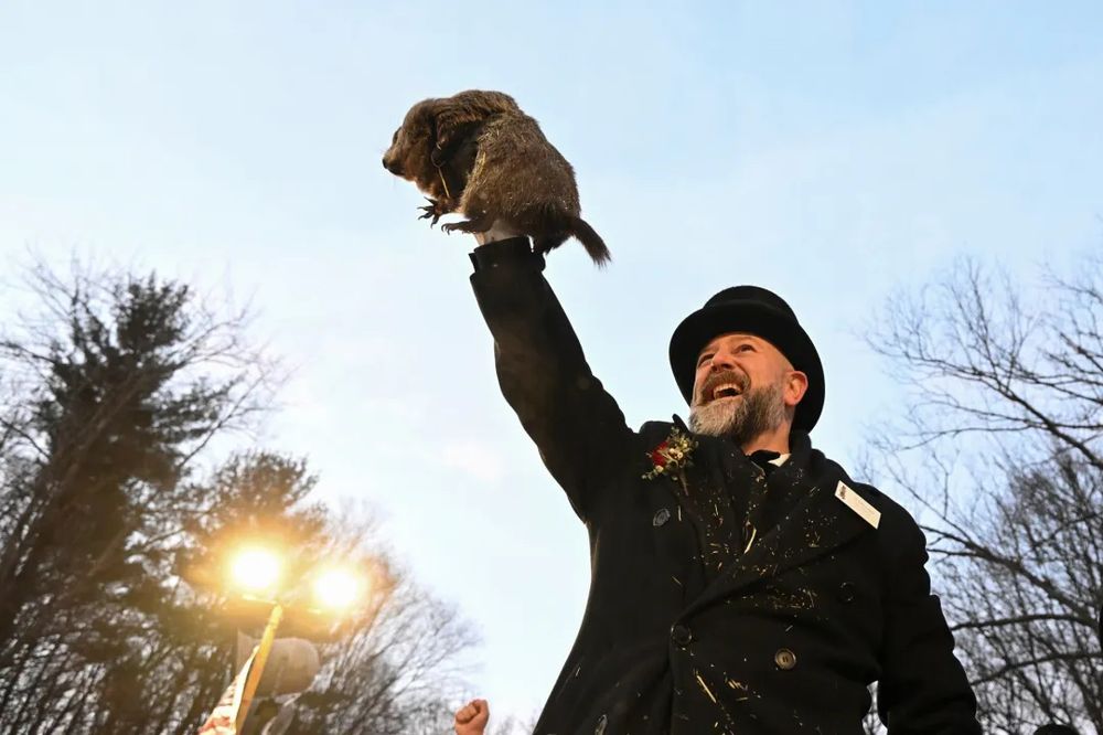 Man in a black suit holding a groundhog into the air 