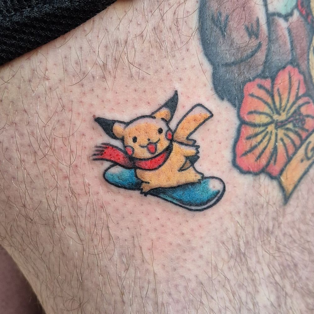 A teeny tiny tattoo of Pikachu riding a snowboard, based on original 90s art published in Japan from the Pokemon Company.