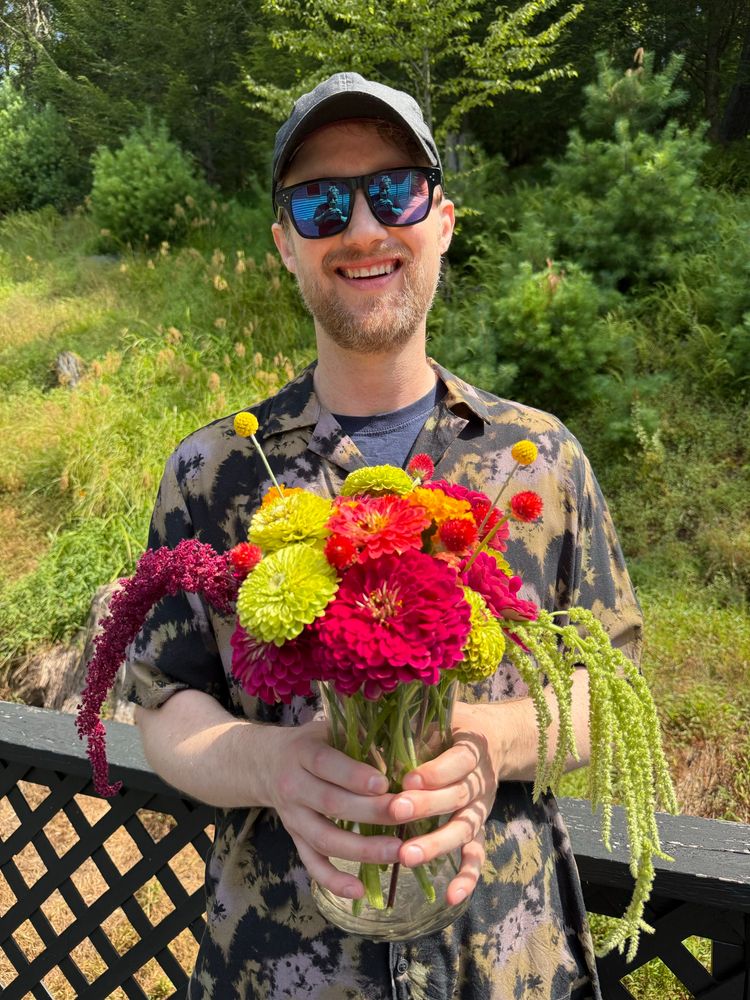 A photo of me holding a flower arrangement with dahlias, zinnias, marigolds, amaranth, Billy buttons and gomphrena 