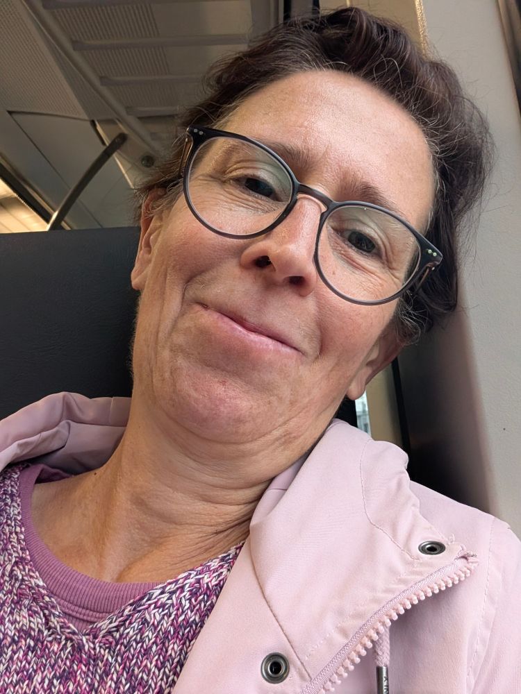 Selfie Ich sitze in der Bahn und lächel in die Kamera. Ich habe einen dunkel pinke Pullover an und einen rosa Anorak. 