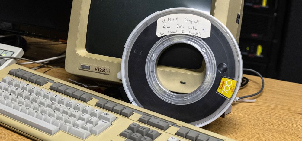 A magnetic tape of UNIX V4 (from 1973) leaned up against a VT220 virtual terminal (from 1983). Photo credit, Dan Hixson, University of Utah