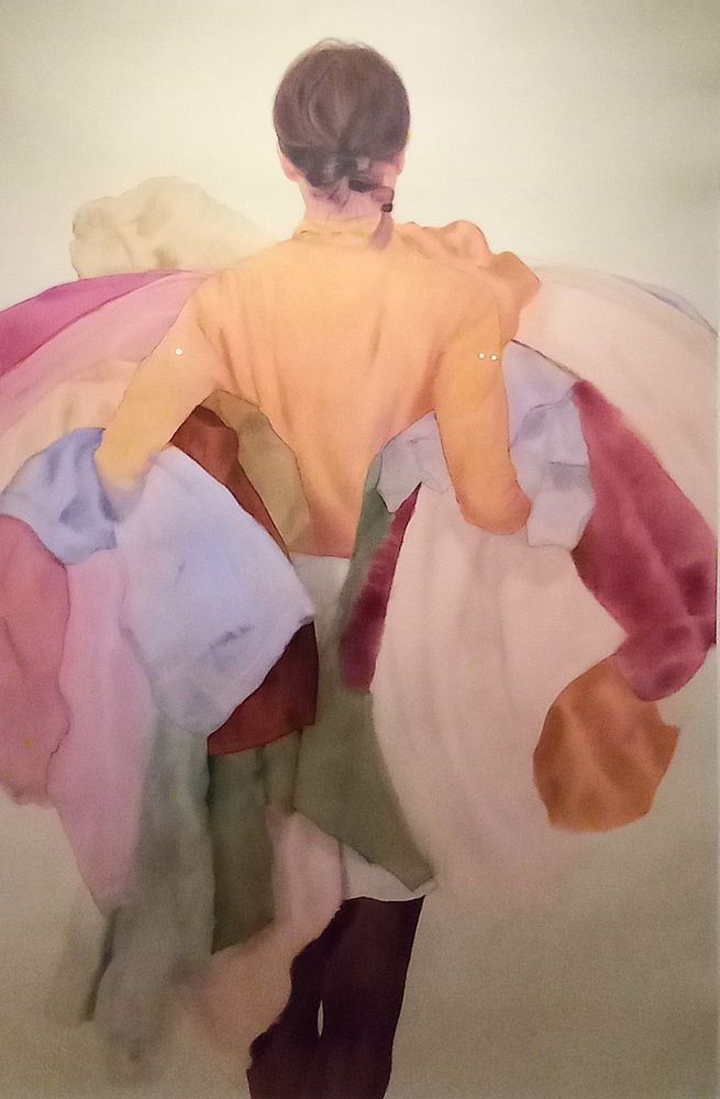 A woman shown from behind carrying a huge pile of linen for the laundry 