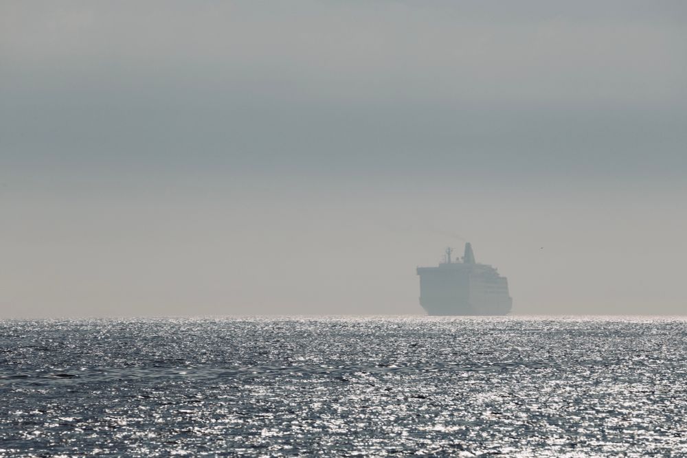 The overnight ferry appears through the morning mist as the hazy sunlight glints on the sea. 