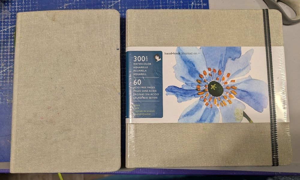 Old art journal laid next to the new unopened journal 