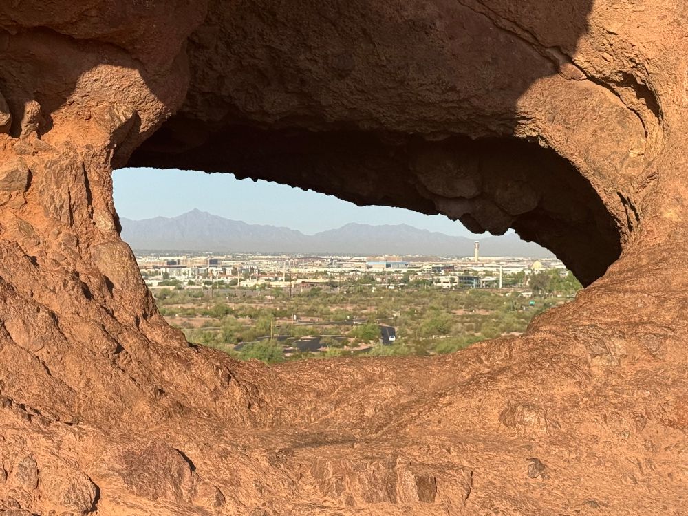 The hole in the rock in Papago Park, Tempe, Arizona in the center of the frame with the cityscape in the distance.