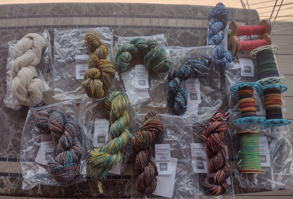 Patio table with nine skeins of yarn and six bobbins of singles ready to ply. Many colors and fibers. Two of the bobbins were turned into finished yarn after this photo was taken.
 