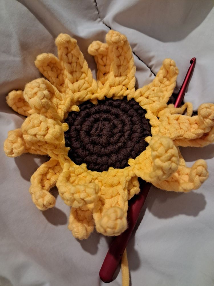 This is my first crochet attempt at a sunflower. It's not great, and the petals keep curling because my stitches are too tight. I left the red crochet hook in the picture because I'm not finished yet. 