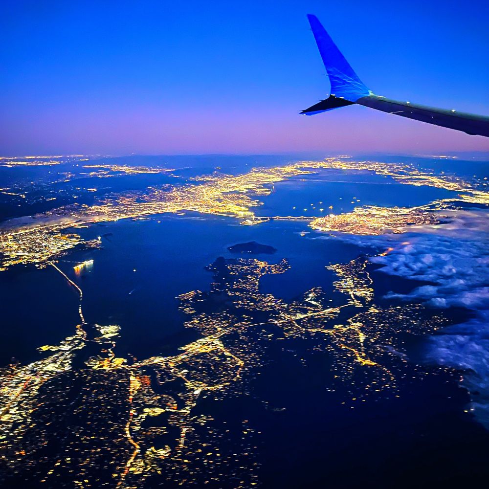 The lights of the SF Bay Area gleam at twilight as seen from an airplane window