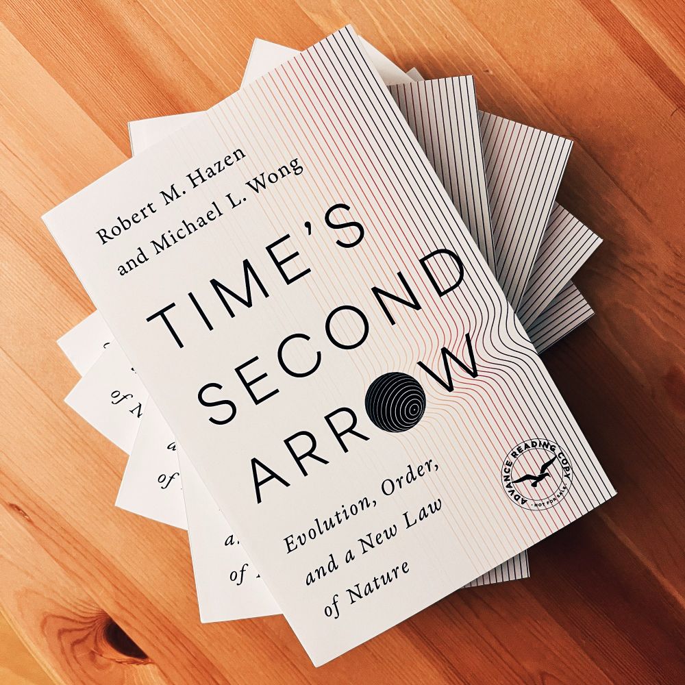 A stack of “Time’s Second Arrow: Evolution, Order, and a New Law of Nature” by Robert M. Hazen and Michael L. Wong sits on a wooden table