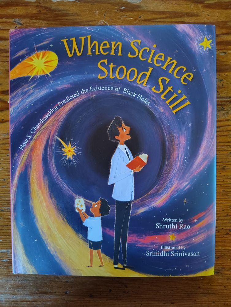 Book cover showing a young boy and a young man against a background of space and stars in blues, golds, and pink Title: WHEN SCIENCE STOOD STILL: HOW S. CHANDRASEKHAR PREDICTED THE EXISTENCE OF BLACK HOLES. Author: Shruthi Rao; Illustrator: Srinidhi Srinivasan