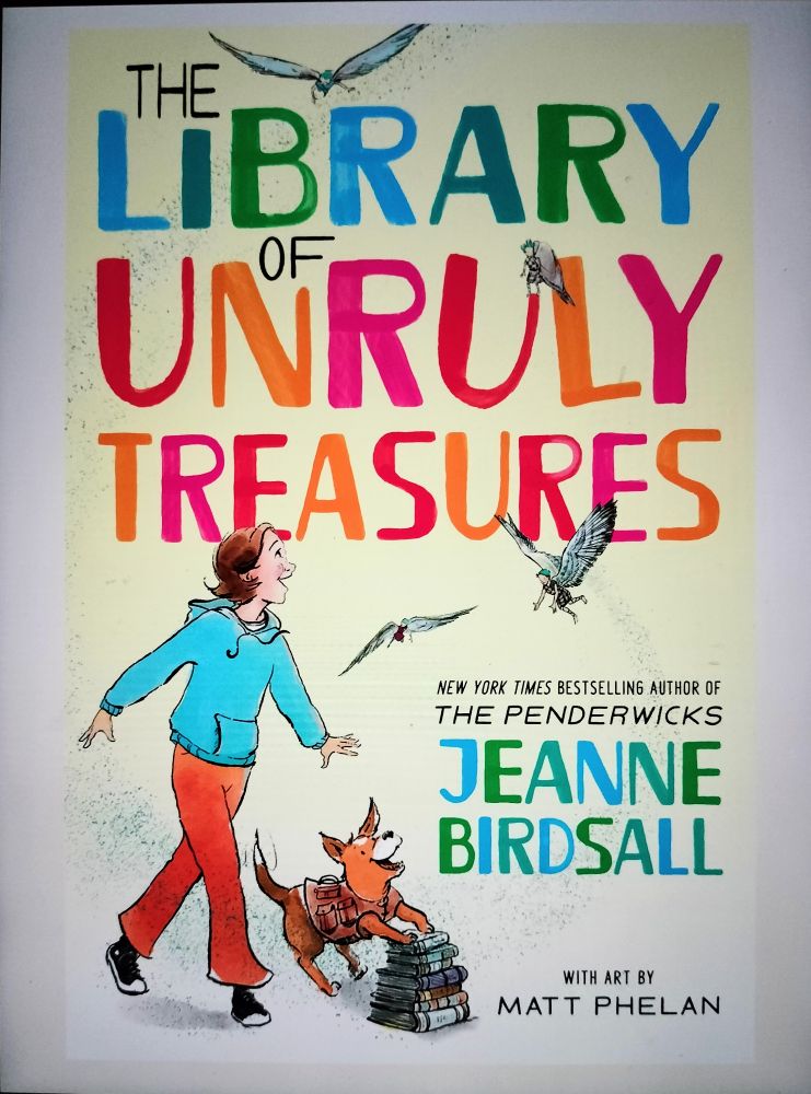 Book cover with a white background and colors of blue, red, and green. A girl walks along with Lahdukan flying around her and a dog with its front paws on top of a stack of books. 