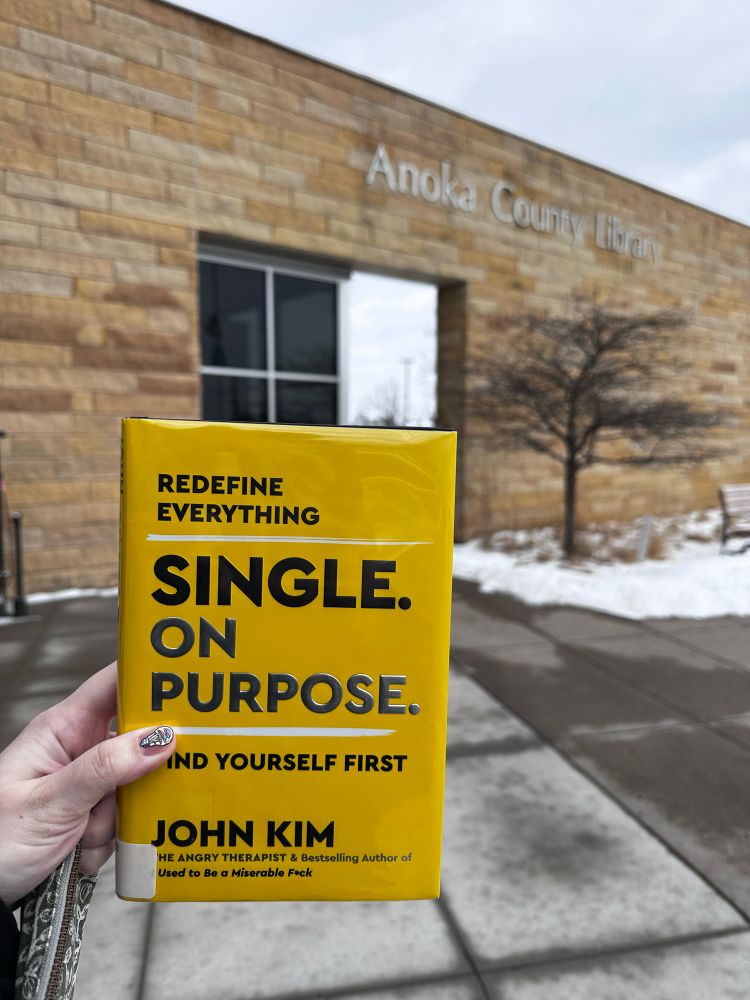 Front cover of “Single on Purpose: Find Yourself First” by John Kim. I’m holding it in front of the outside of my library. There’s snow on the ground.