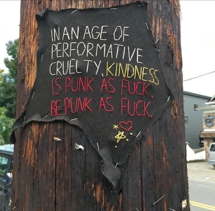 Poster on a wooden pole saying: in the age of performative cruelty, kindness is punk as fuck, be punk as fuck.