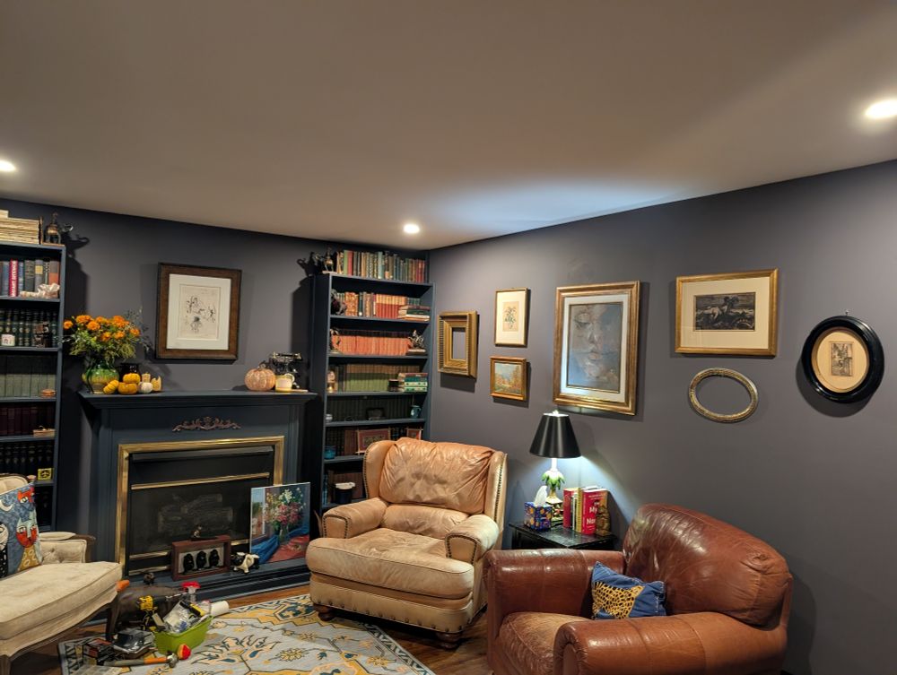 Room with bookshelves, paintings two letter chairs and a pattern yellow and blue rug.