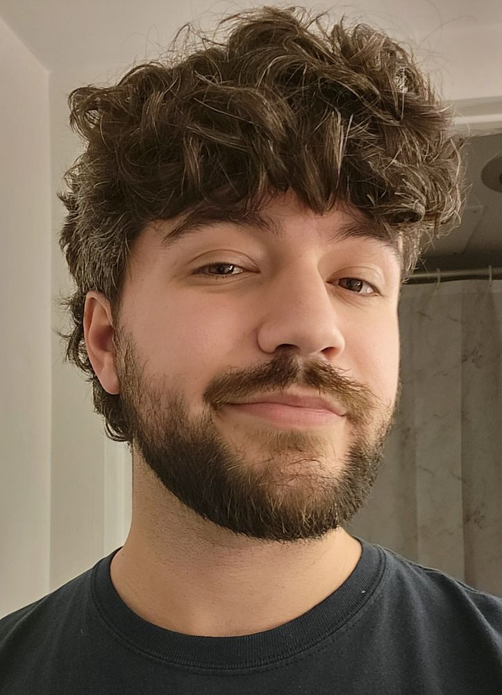 A 31-year-old man with loosely curly brown hair. He's growing it out more in the back after having only had the curls on top for a while. His hair is shorter and greyer near his hears.