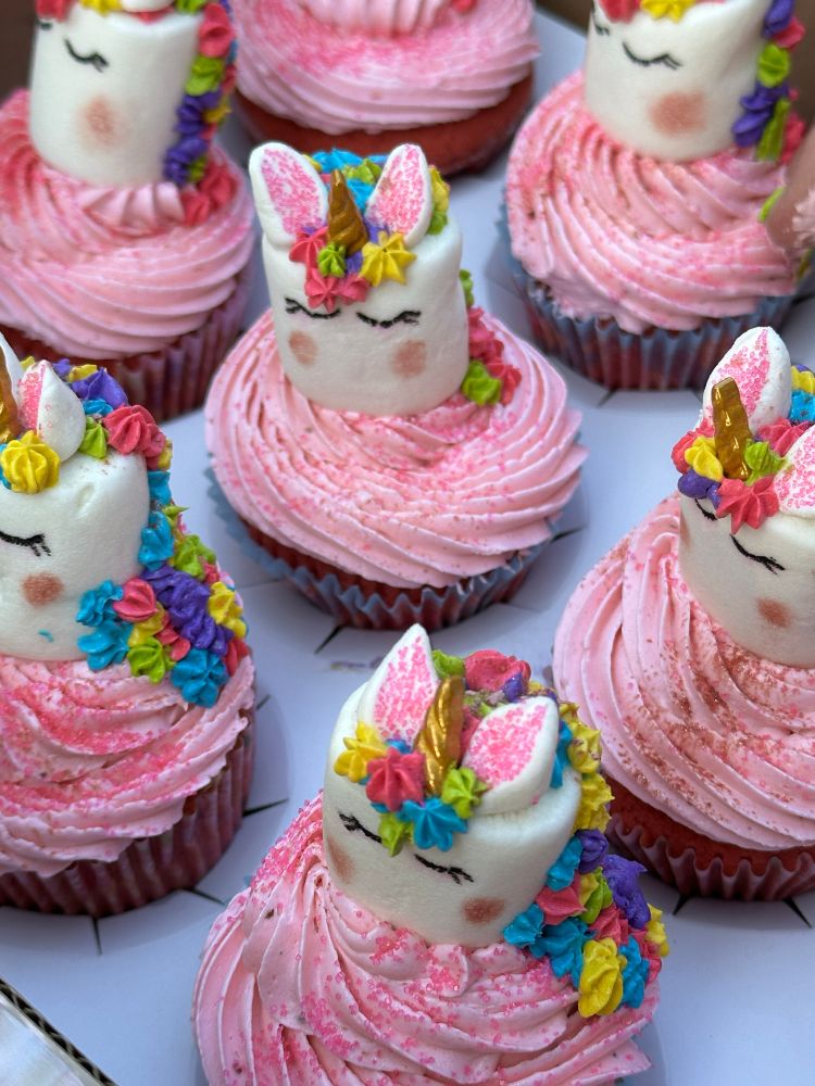 Pink cupcakes swirled with pink frosting and topped with a marshmallow unicorn with a golden horn and rainbow mane. 