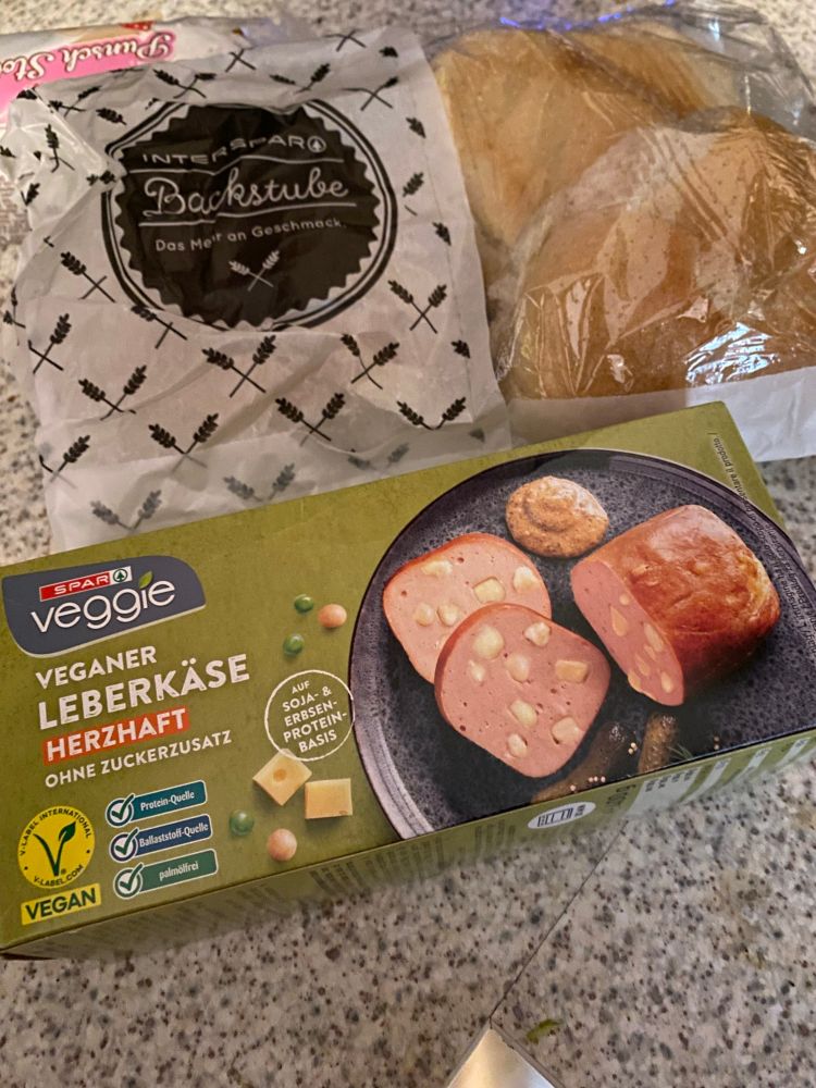 Eine Packung vegaber Käsleberkäs vom Spar, dabei ein Papiersackerl mit Semmeln