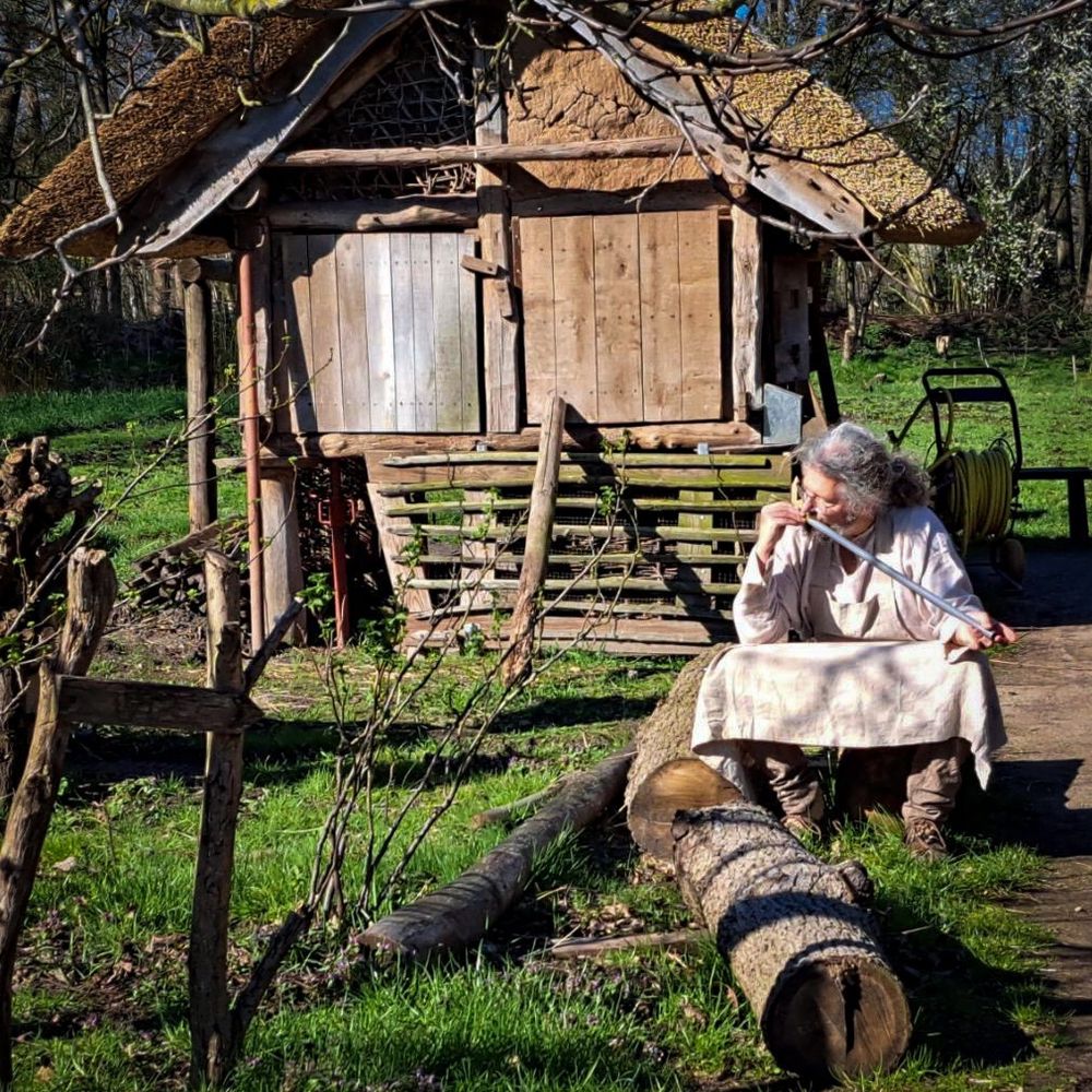 Man in medieval clothes playing the willow flute in front of a medieval farm building