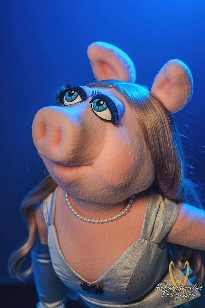A picture of a Miss Piggy replica puppet. Piggy is looking off to the side, with her mouth closed. She is wearing a silver top, with purple gloves, and has long blonde curly hair. 