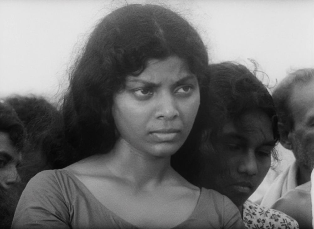 different young woman with dark top looking slightly to her left, looking concerned, other women in background