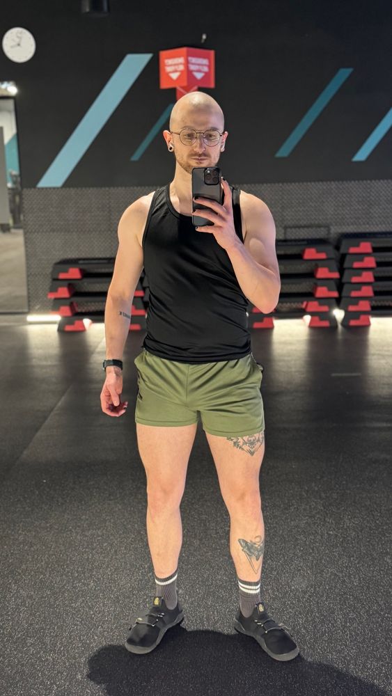 A selfie of me at the gym. I’m wearing a black vest and khaki shorts. 