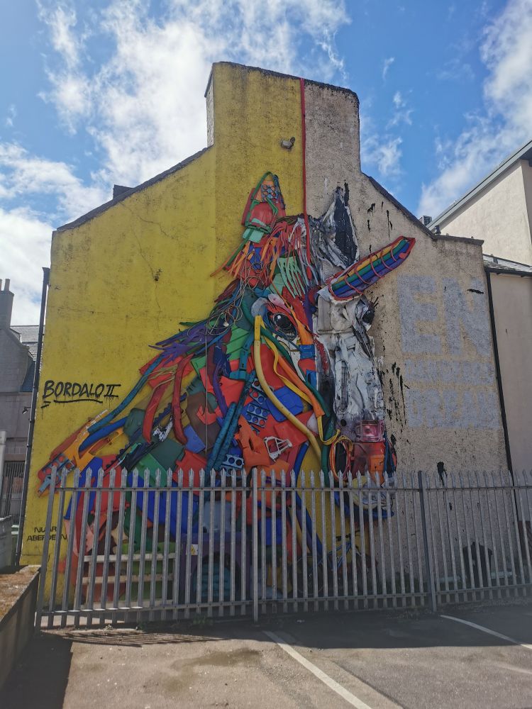 A rainbow-coloured unicorn constructed from trash materials on the end of a building on the NUART trail