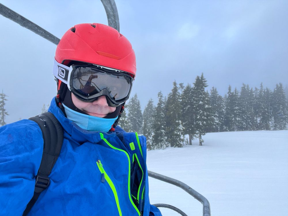 A man on a ski lift in a blue coat and orange helmet 