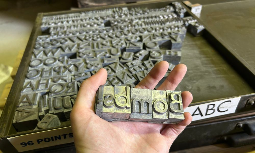 Cold metal lead type with the word “bombs” in a large display size of the typeface Futura, designed by Paul Renner in 1929