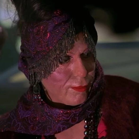 A woman named Kyvan from an episode of the tv show Farscape who had a terrible Jamaican accent looking to the side while wearing a red and purple scarf.