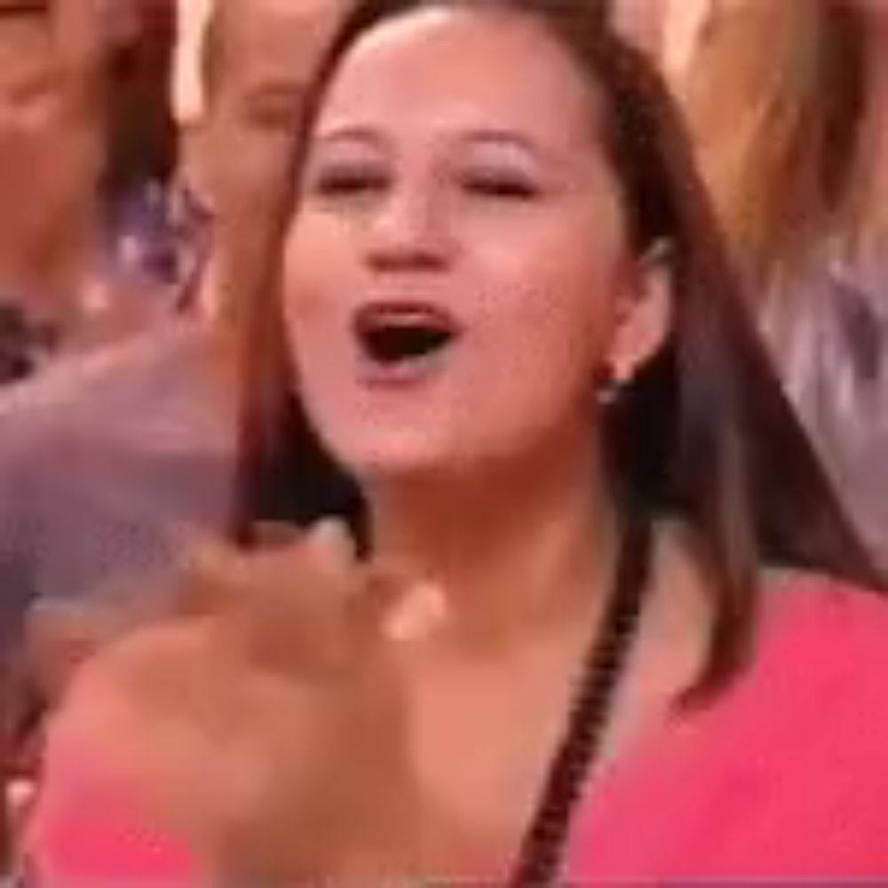 a woman is applauding in a crowd of people while wearing a pink shirt .