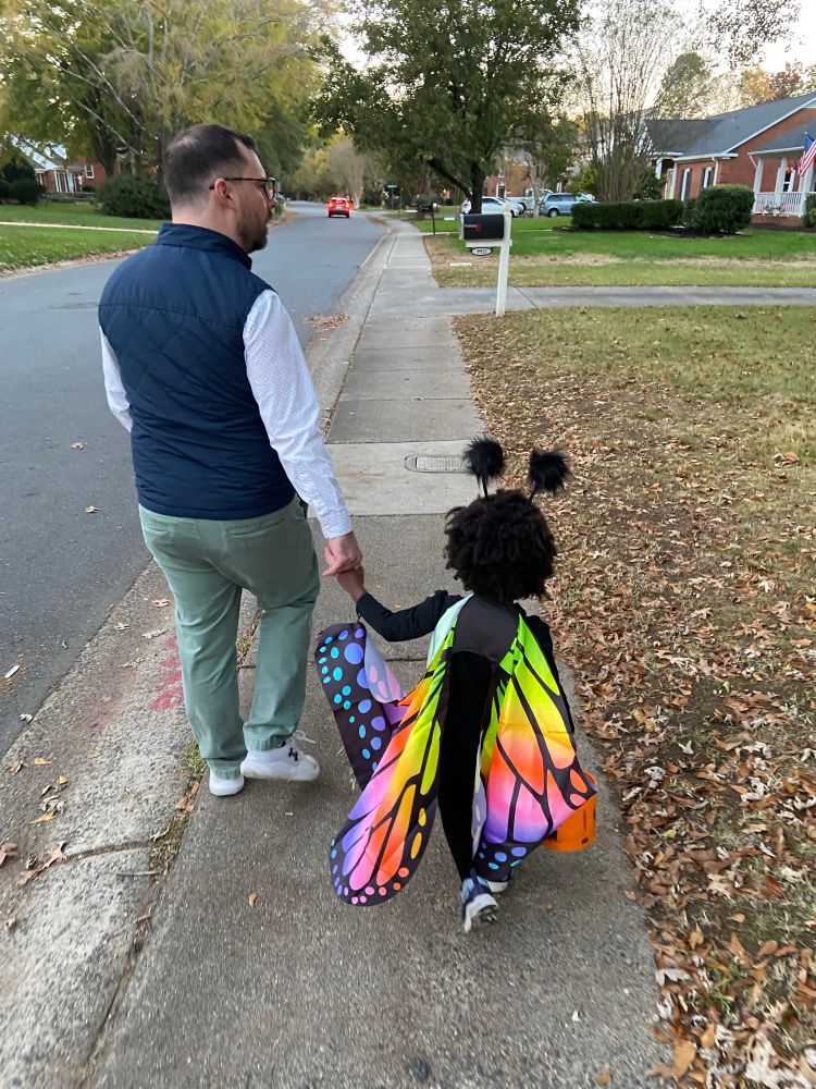A man walking a little girl dressed as a butterfly down a residential street.