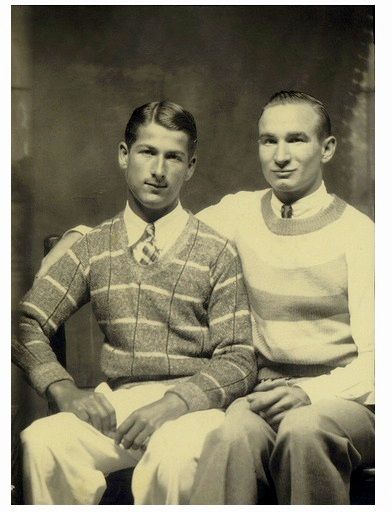 2 chummy men posing at a photographer's studio wearing their best ties and nice sweaters.  Maybe the 1920s or 30s.