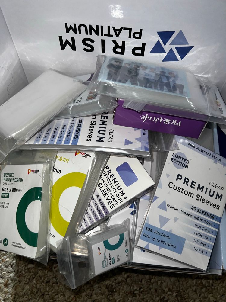 Different sizes of photocard sleeves inside a box. Some sleeves are labeled Popcorn, Meowcafe and Prism Platimun Premium Custom sleeves. 