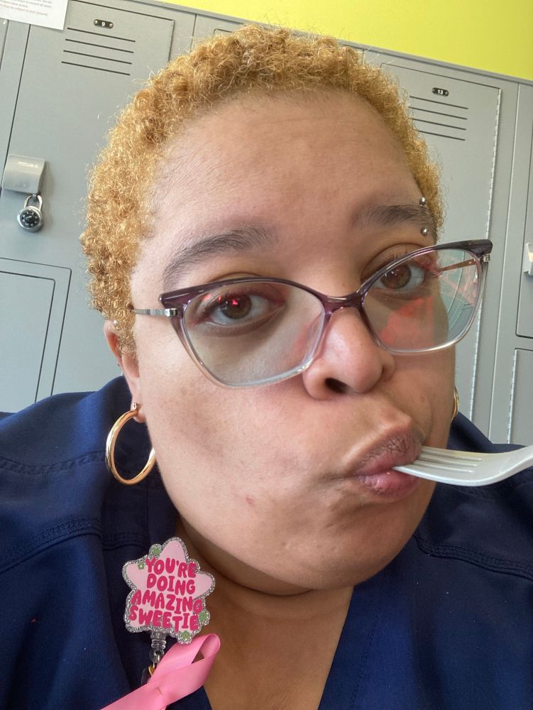 Indie is eating lunch. The fork still in her mouth. She had a badge reel that reads “YOU’RE DOING AMAZING SWEETIE” with a pink ribbon. 

Her hair has changed and is now somewhere between red and strawberry blonde. 